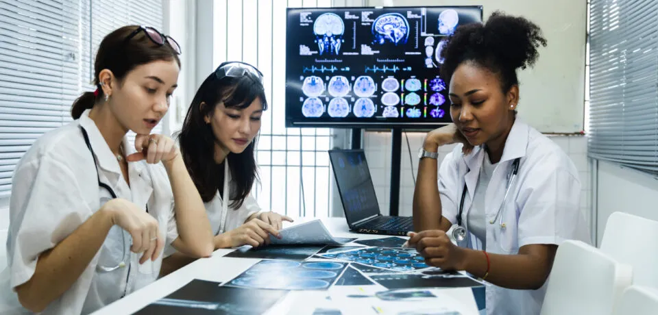 Team of female doctor check on scan results paper and looking at Team of female doctor check on scan results paper and looking at monitors in laboratory and plan and share medical knowledge and experience benefits her coworkers and patients