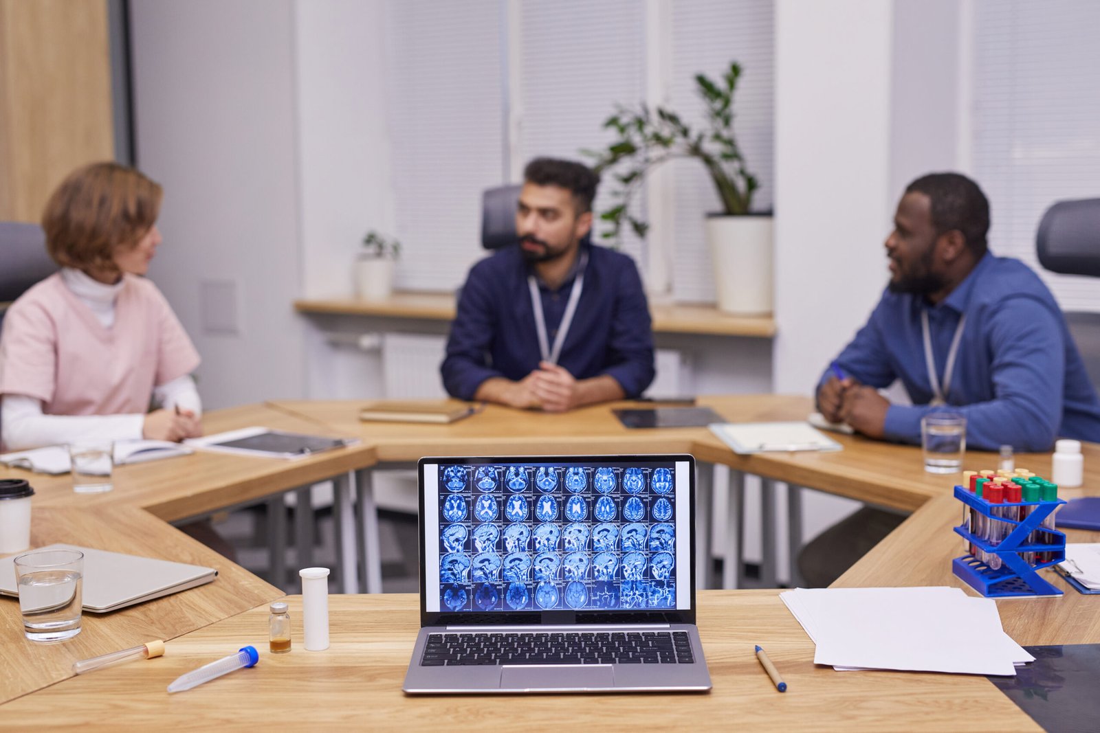 Brain scan on laptop screen on background of three young intercultural medical experts brainstorming and discussing new strategies