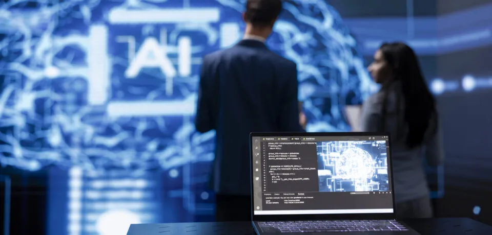 Focus on laptop running AI cognitive computing tech used by IT staff members Focus on laptop running AI cognitive computing tech used by IT staff members in blurry background. Close up of notebook used by teamworking engineers to do data mining with self learning algorithms