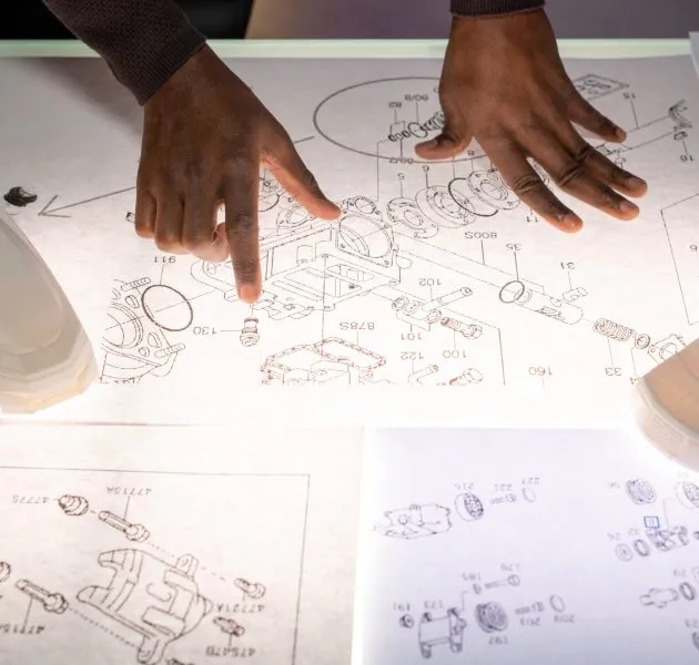 Above view of black automotive engineer standing at desk with car models and analyzing sketches