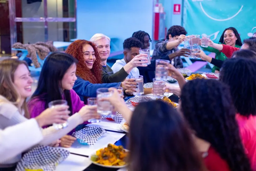 Happy multi ethnic friends raising glasses of water and toasting while sitting at a restaurant table, celebrating together