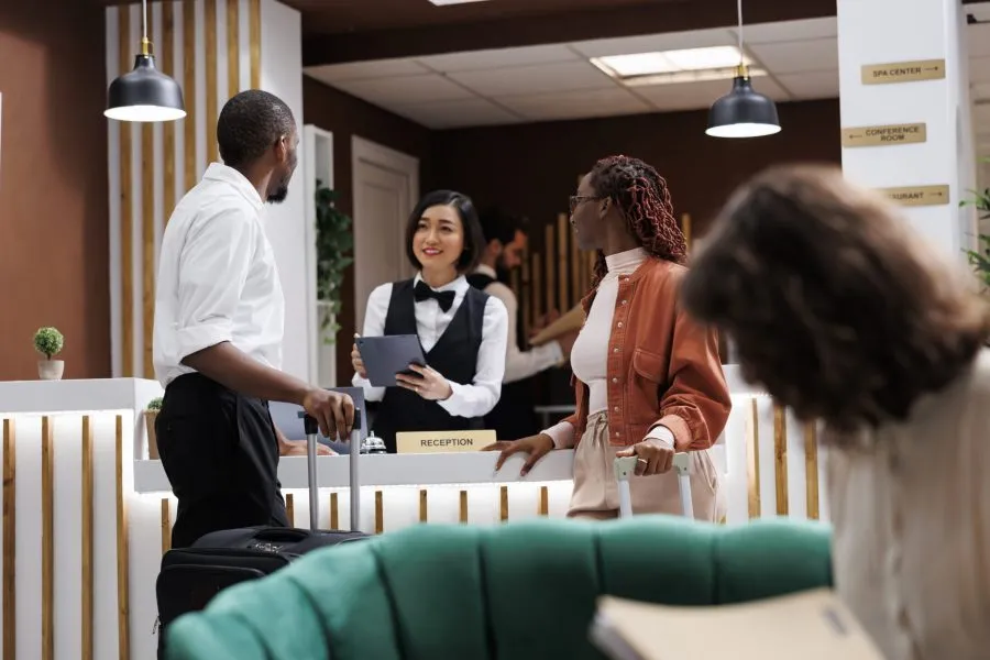 Hotel worker filling in report forms on tablet, providing luxury service with check in process in lobby. Receptionist talking to guests about booking details and room accommodation.