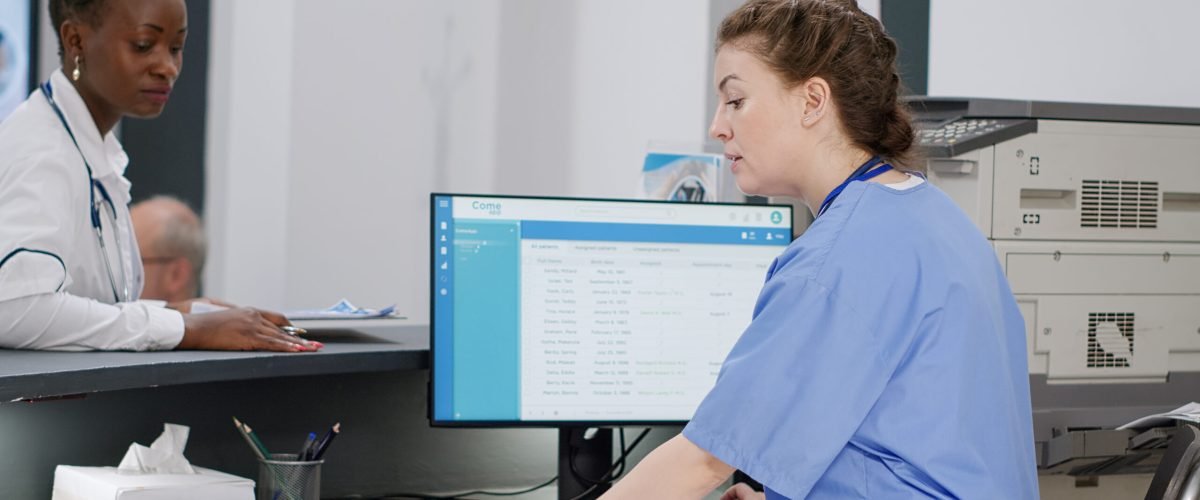 Medical assistant working on patient appointments at reception desk, helping african american doctor with information to do consultation with senior man. Diverse staff at healthcare clinic.