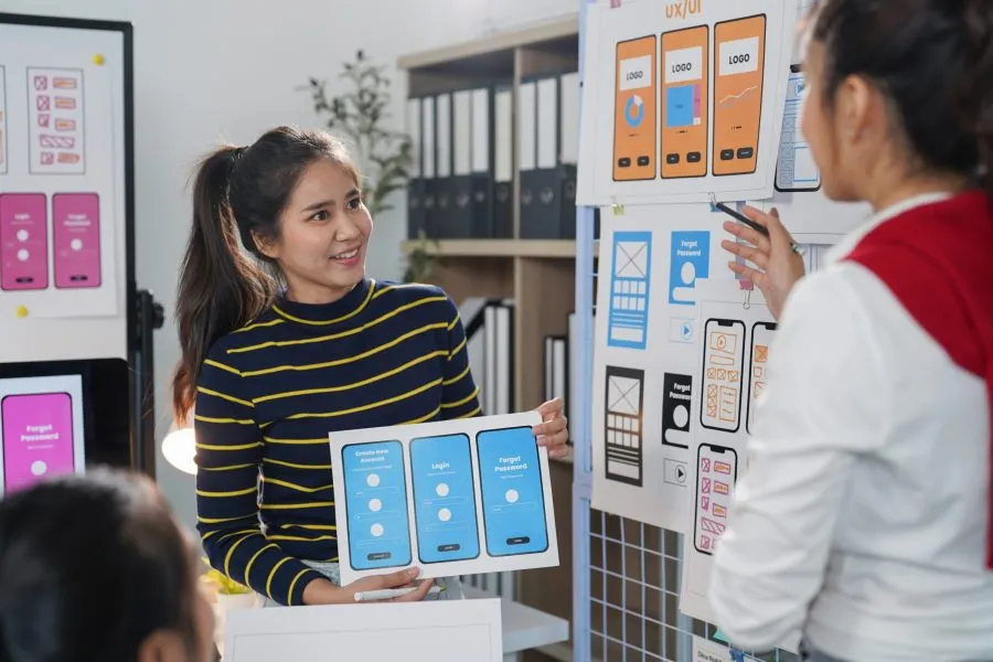 Two female web designers collaborating on user interface and user experience for a mobile application, engaging in discussions and brainstorming ideas in a modern office setting
