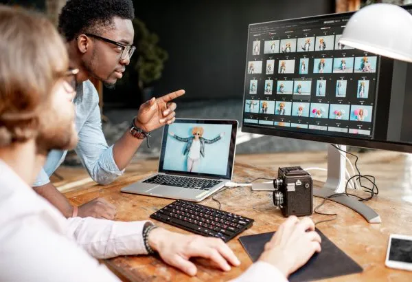 Two male photographers choosing woman's portraits at the working place with two computers in the studio